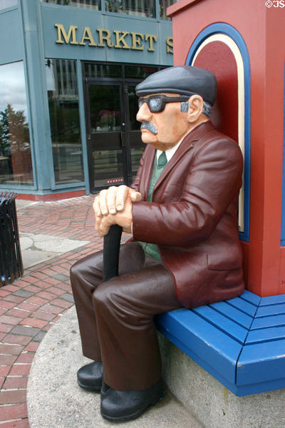 Sculpted senior with cap & horn rims sitting at base of Timepiece Clocktower. Saint John, NB.