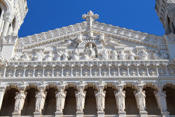 Carving of citizens kneeling before Virgin Mary in pediment over row of carved angels on facade of Basilique Notre-Dame de Fourvière. Lyon, France.