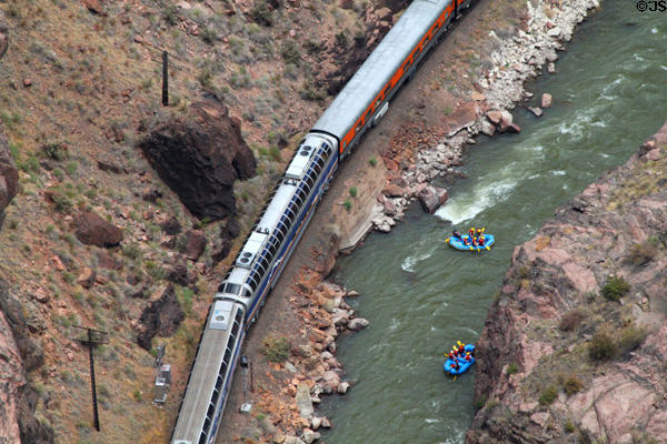 Observation cars of Royal Gorge Route Railway pass rafters on Arkansas River in Royal Gorge. CO.
