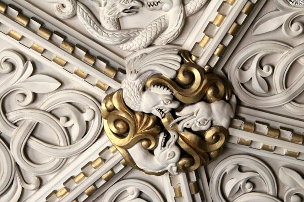 Detail of gilded medallion with intertwined sculpted plaster figures on ornate ceiling in Library at Penrhyn Castle. Bangor, Wales.
