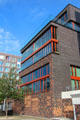 Modern building with red trim around windows where decorative brick of flood barrier has been extended upward on Dalmannkai in HafenCity. Hamburg, Germany.