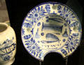 Tin-glazed earthenware barber's bowl painted with comb, scissors & other tools of profession & cutout to fit client's neck by TW of London at Potteries Museum & Art Gallery. Hanley, Stoke-on-Trent, England.